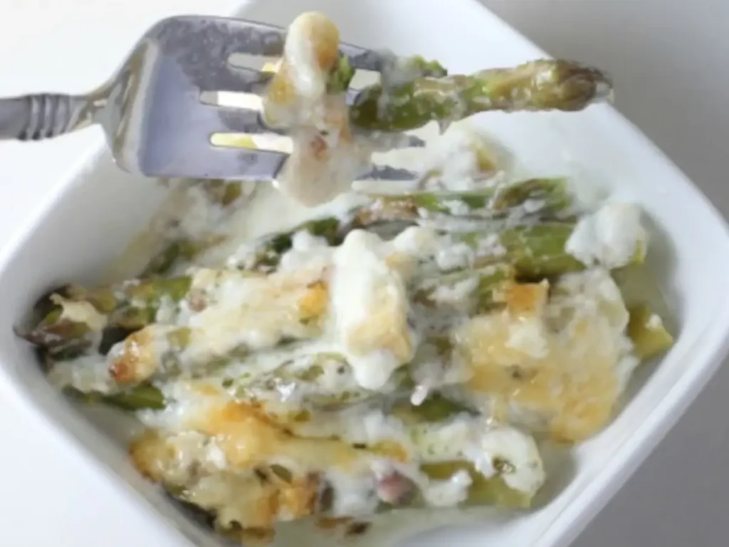 A bite of creamed asparagus with parmesan cheese, in a white bowl, using a fork. 