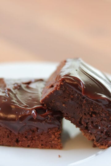 2 brownies with chocolate frosting stacked on a white plate