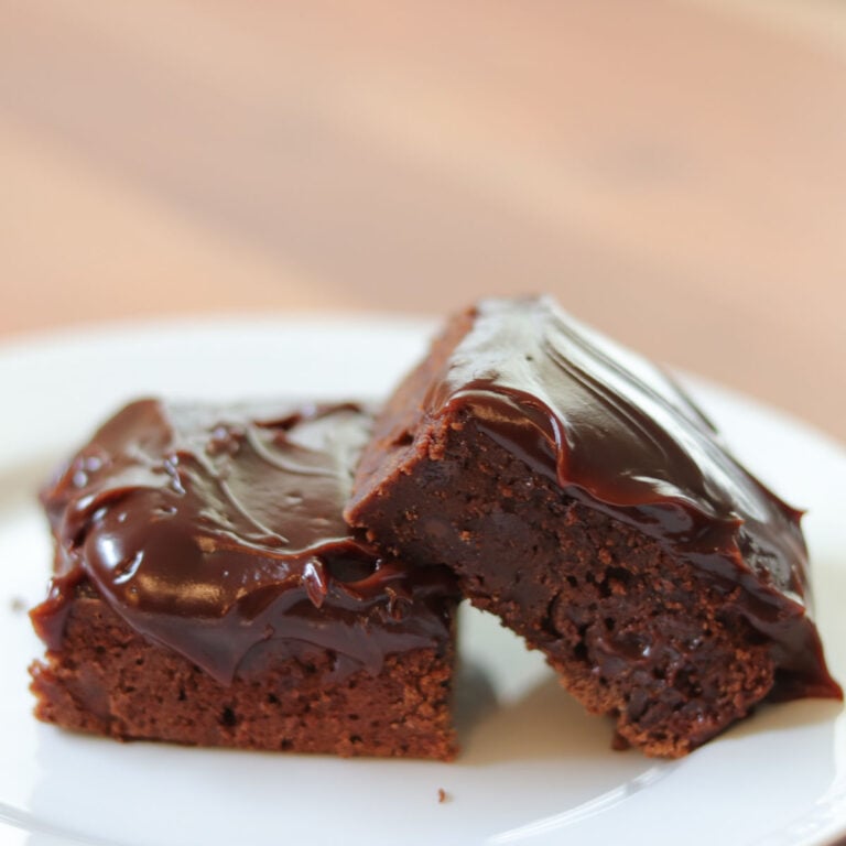 2 brownies with chocolate frosting stacked on a white plate