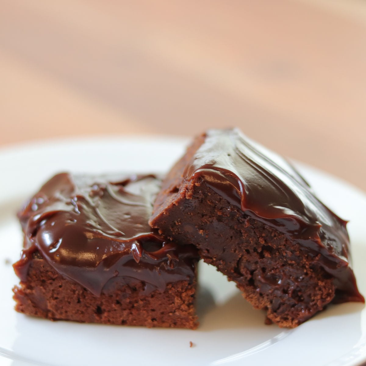 2 brownies with chocolate frosting stacked on a white plate