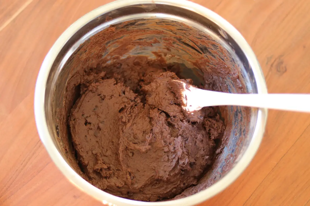 Wet ingredients added to dry ingredients in a mixing bowl with a spatula. 