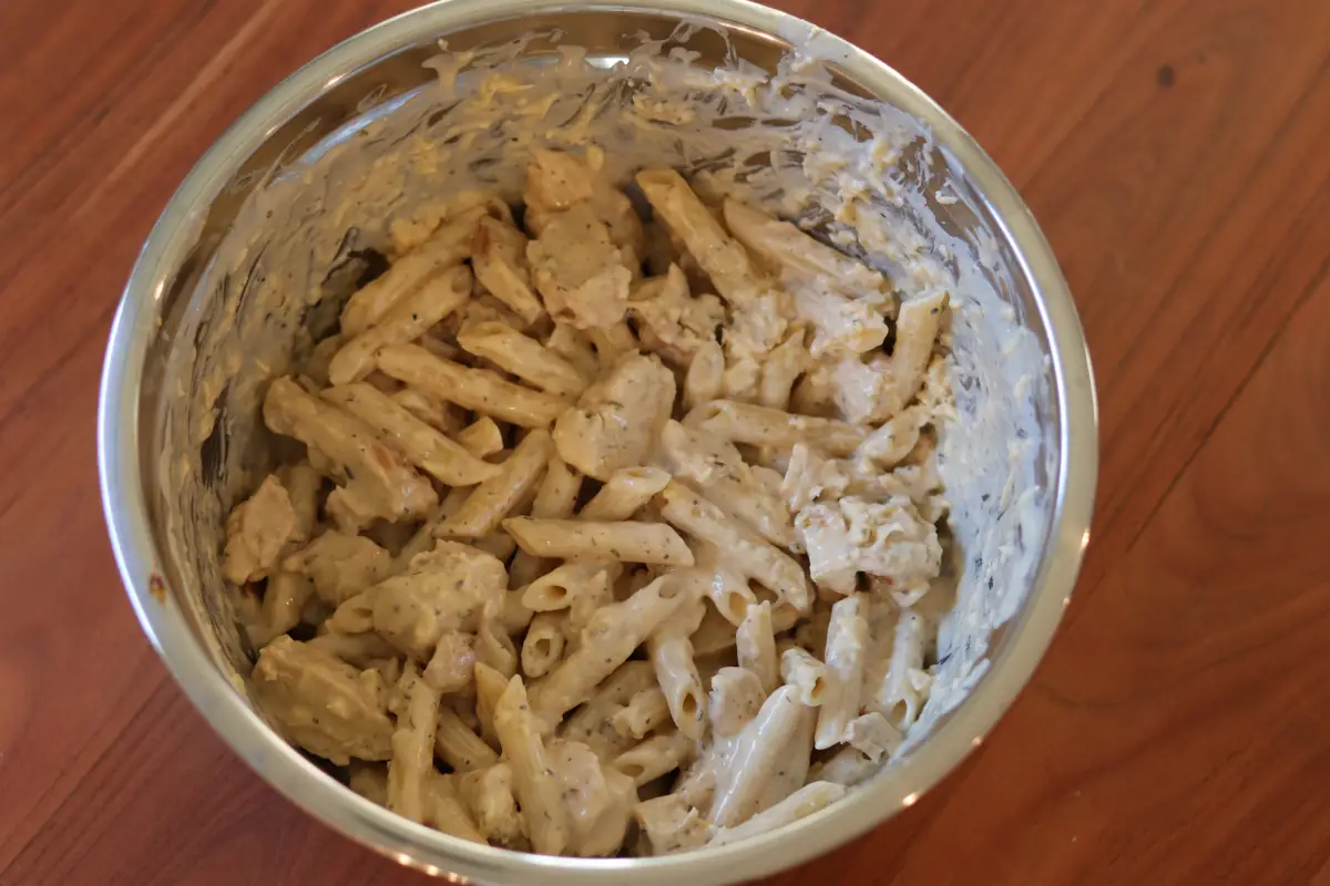 Pasta, chicken, alfredo sauce, seasonings, and cheese, mixed together in a mixing bowl. 