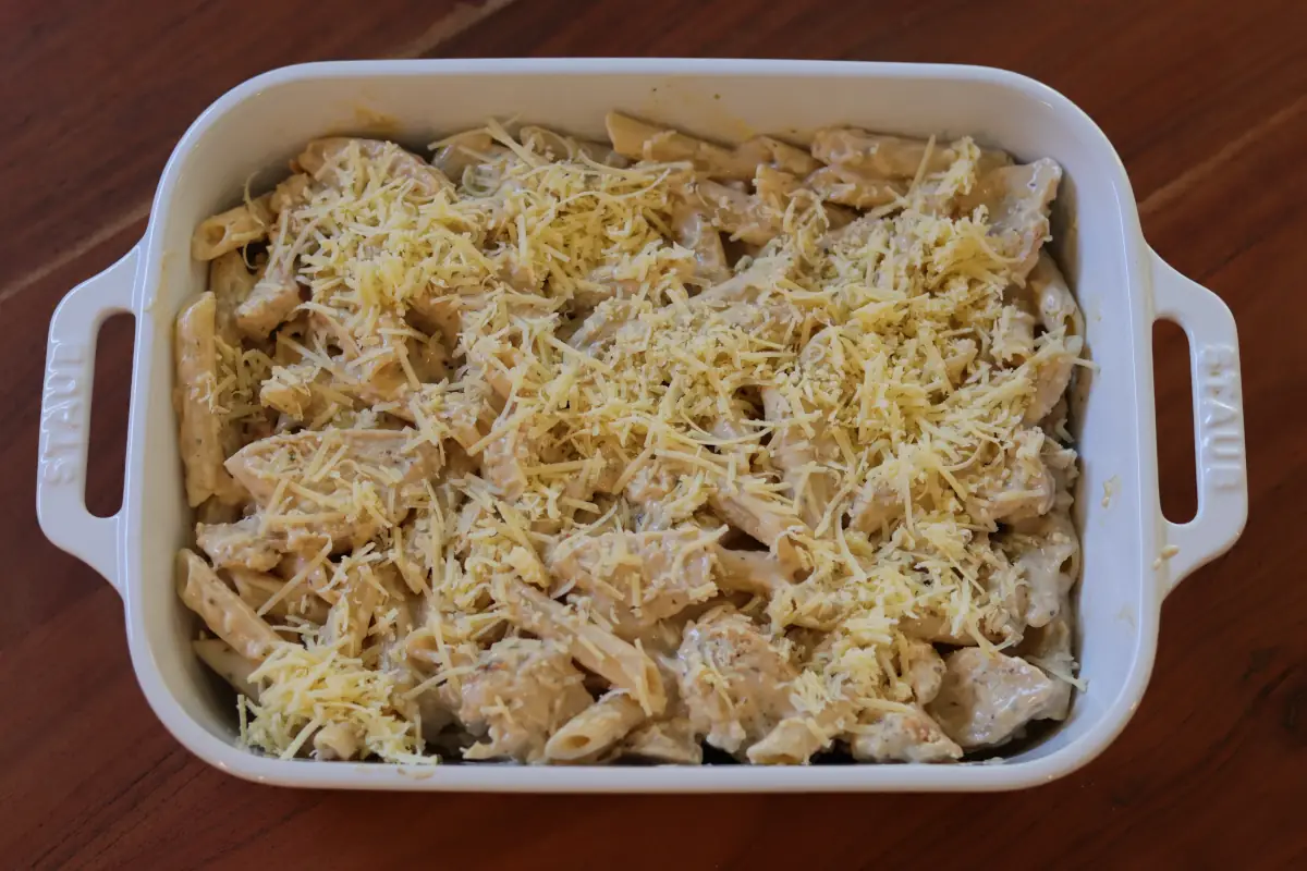 Chicken alfredo in a white baking dish, topped with cheese. 