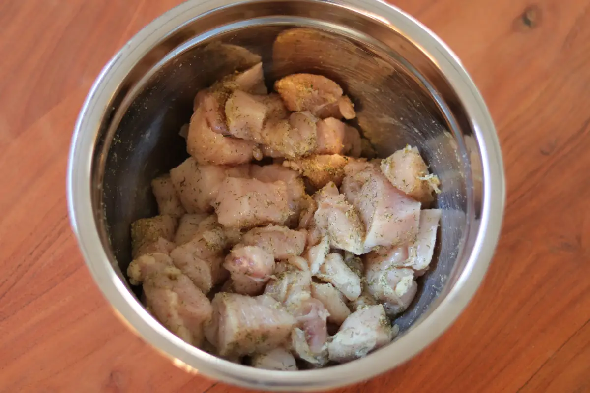 Raw chicken breast seasoned with ranch seasoning, in a stainless steel bowl.