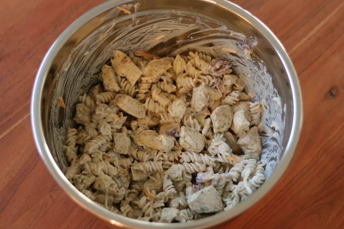 Chicken, pasta, alfredo sauce, greek yogurt, bacon, and cheese combined in a bowl.