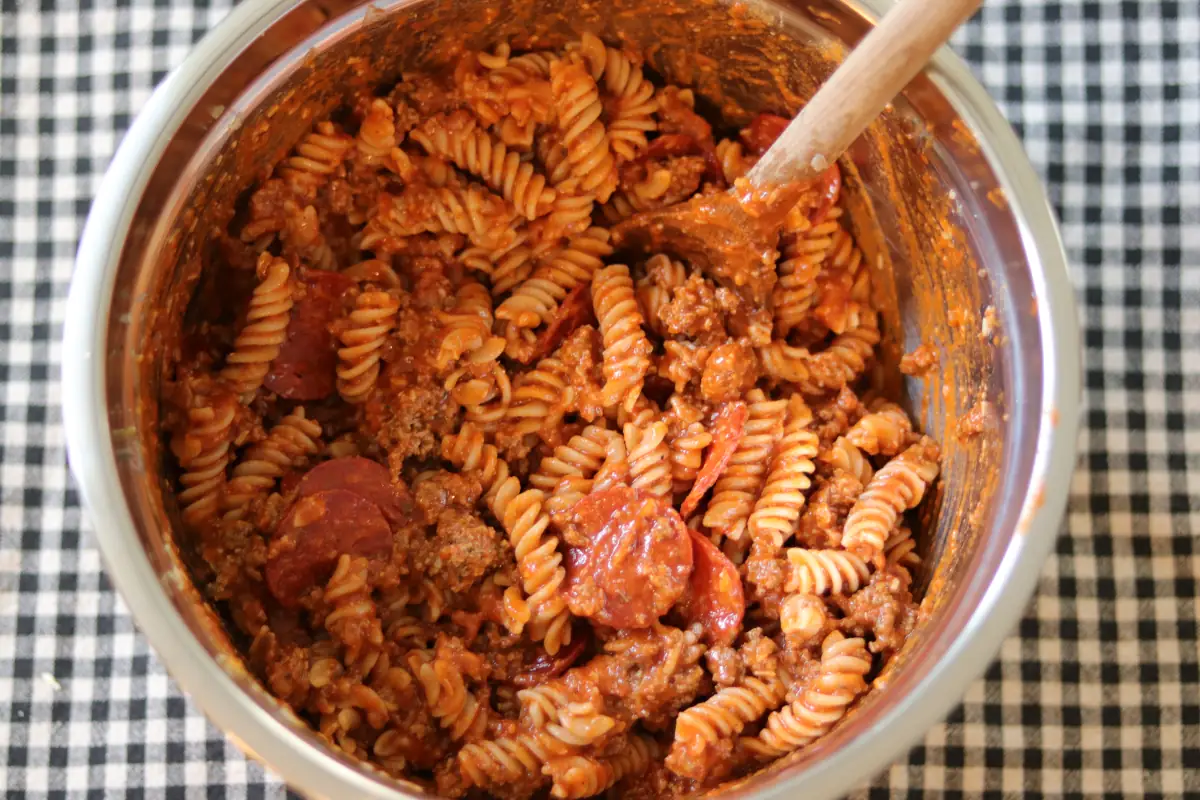 Pasta, pepperoni, pizza sauce, ground beef, and cheese in a mixing bowl.