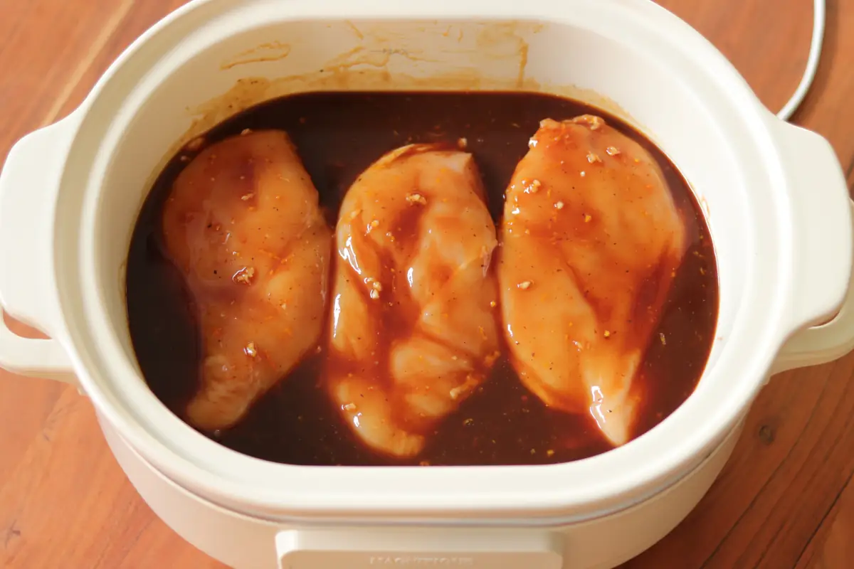 Raw chicken covered with citrus sauce in a slow cooker.