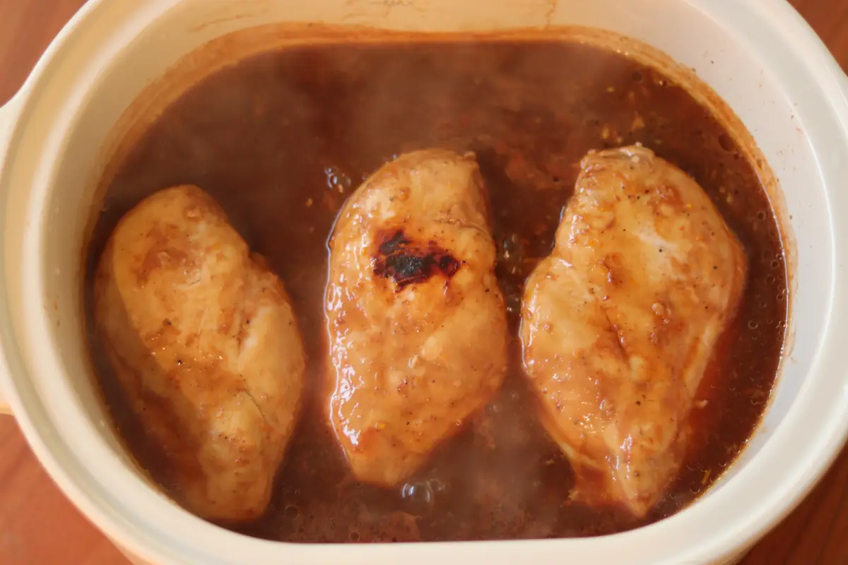 Cooked chicken in the citrus sauce in the slow cooker.