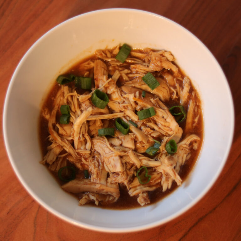 Slow cooker citrus chicken in a bowl garnished with green onions.