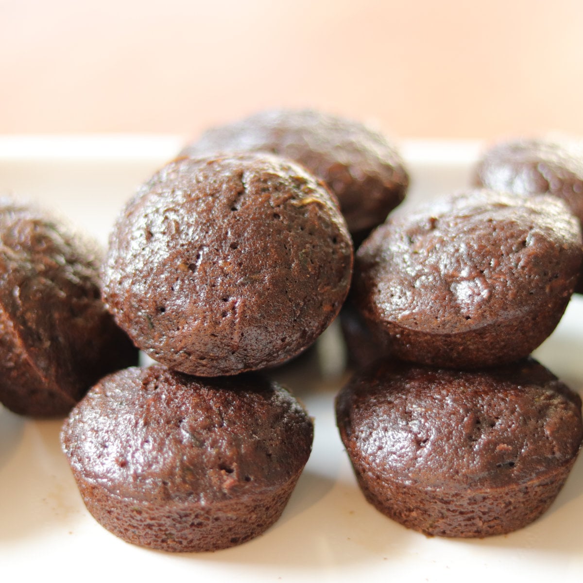 Chocolate Zucchini Mini Muffins stacked on top of each other on a white platter.