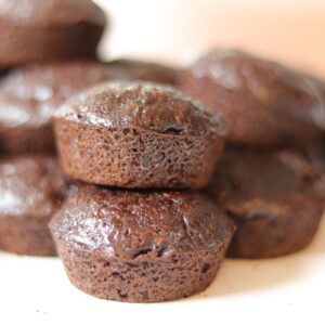 Close up photo of 2 zucchini mini muffins, with muffins behind them.