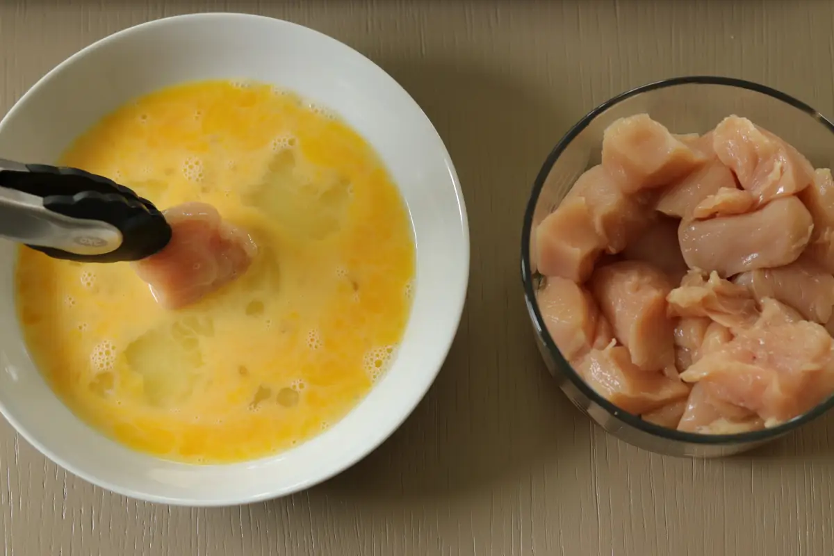 Chicken being dipped into the egg mixture.