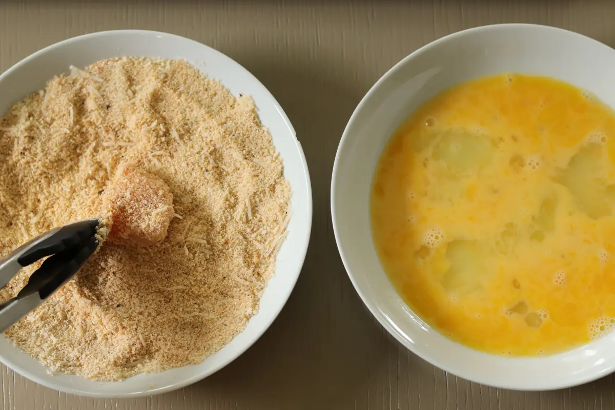 Chicken being dipped into the almond flour mixture.