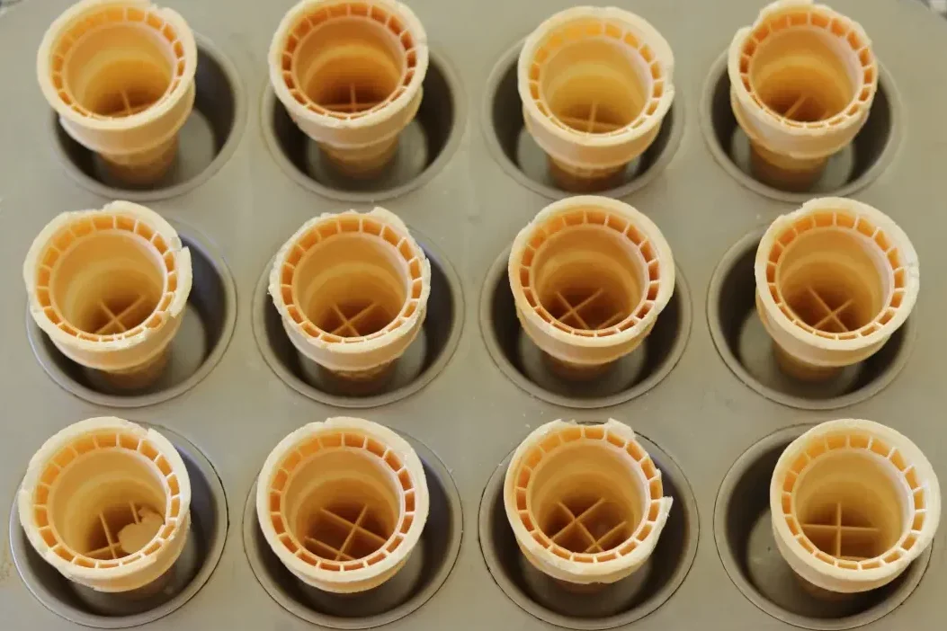 Empty ice cream cones in a muffin tin.
