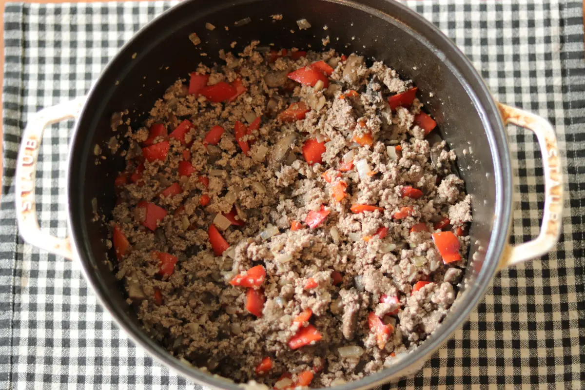 Browned meat and vegetables in a white dutch oven.