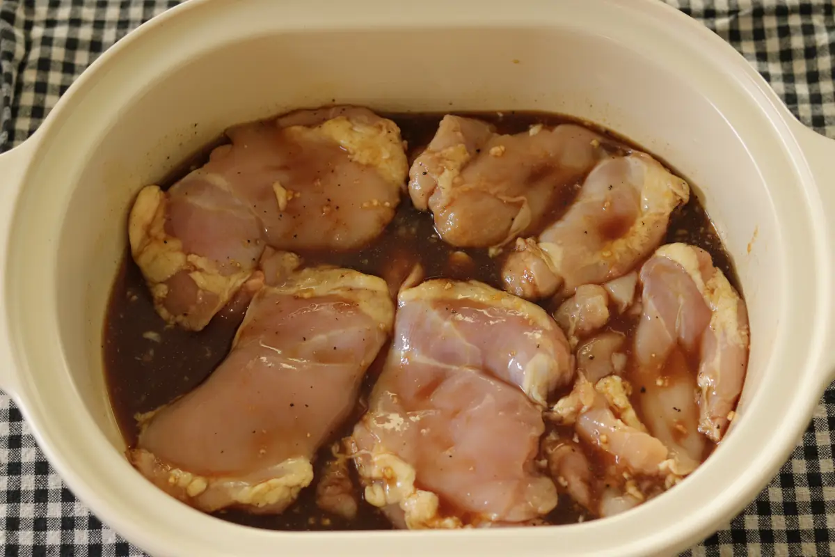 Teriyaki sauce poured over chicken thighs in a slow cooker.