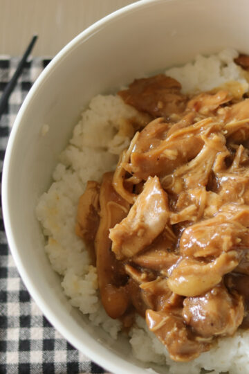 Slow cooker chicken teriyaki over a bed of rice on a plaid towel next to chopsticks.