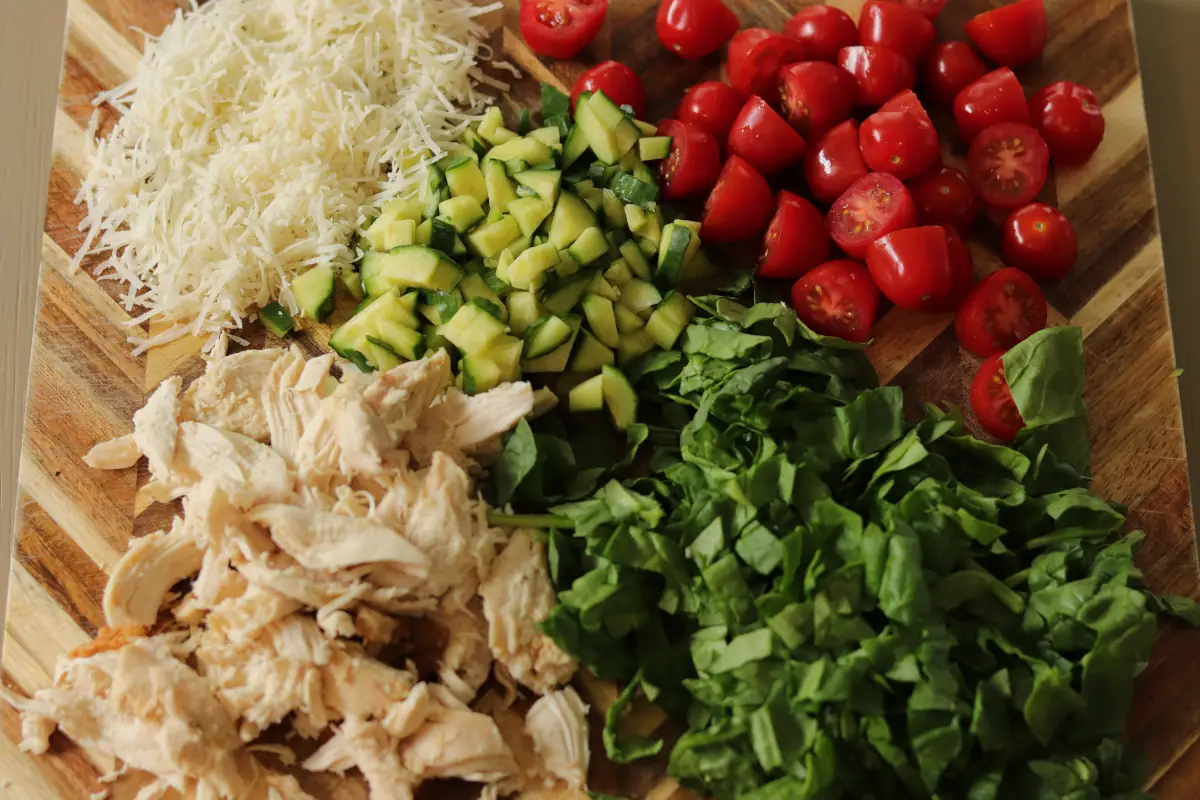 Chopped chicken, cut vegetables, and grated cheese on a cutting board. 